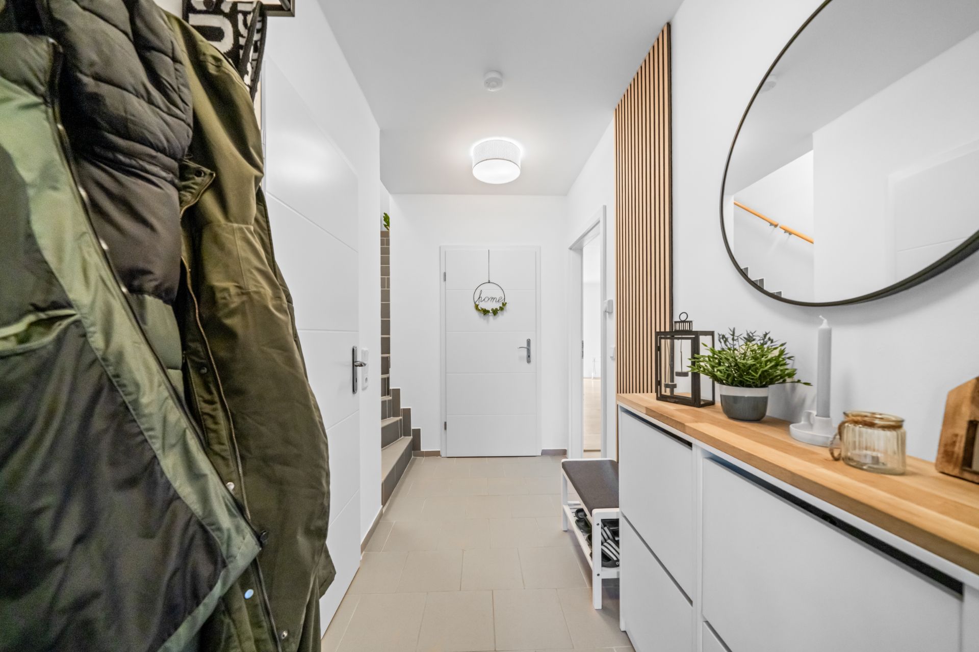 Heller Flur mit Garderobe, Holzkommode, rundem Spiegel und Treppe im Hintergrund.