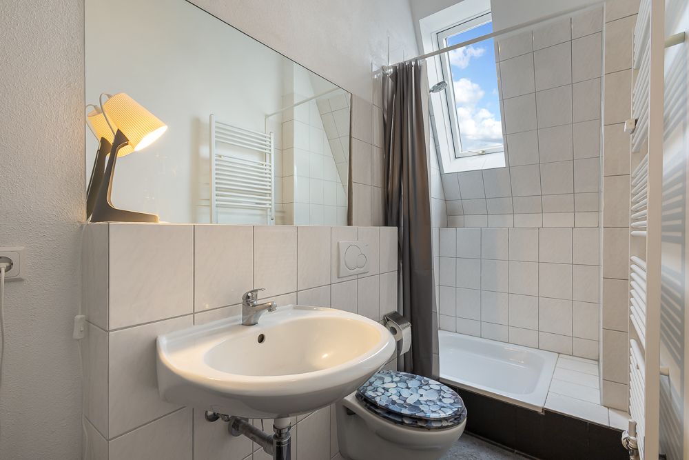 Helles Badezimmer mit Waschbecken, Toilette, Dusche, großem Spiegel und Fenster.
