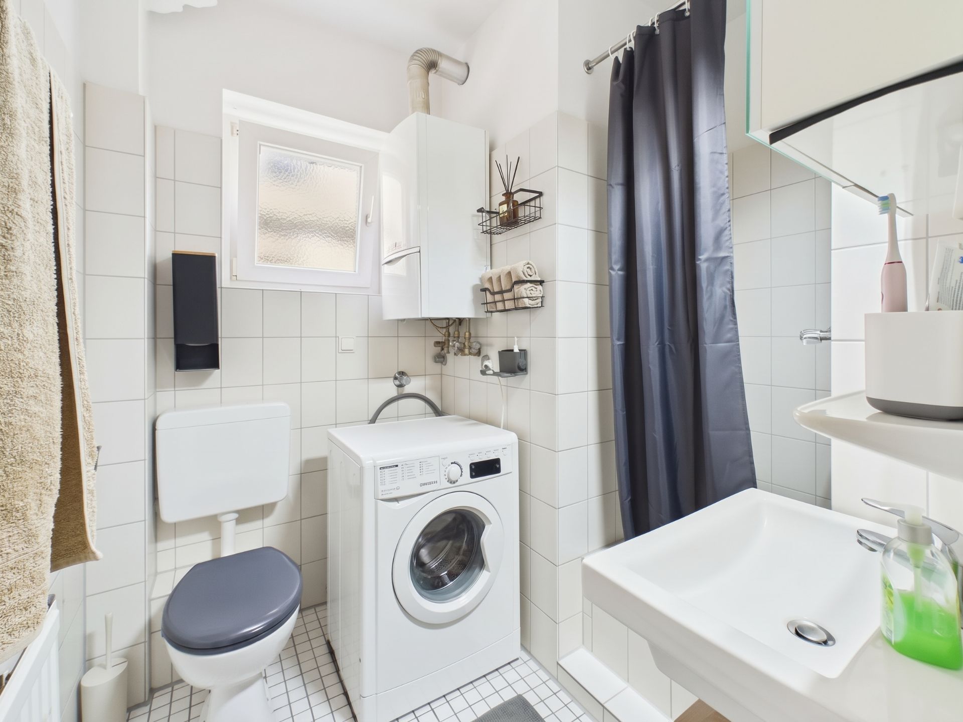 Kleines Badezimmer mit Waschmaschine, Toilette, Waschbecken und Dusche mit dunklem Vorhang.