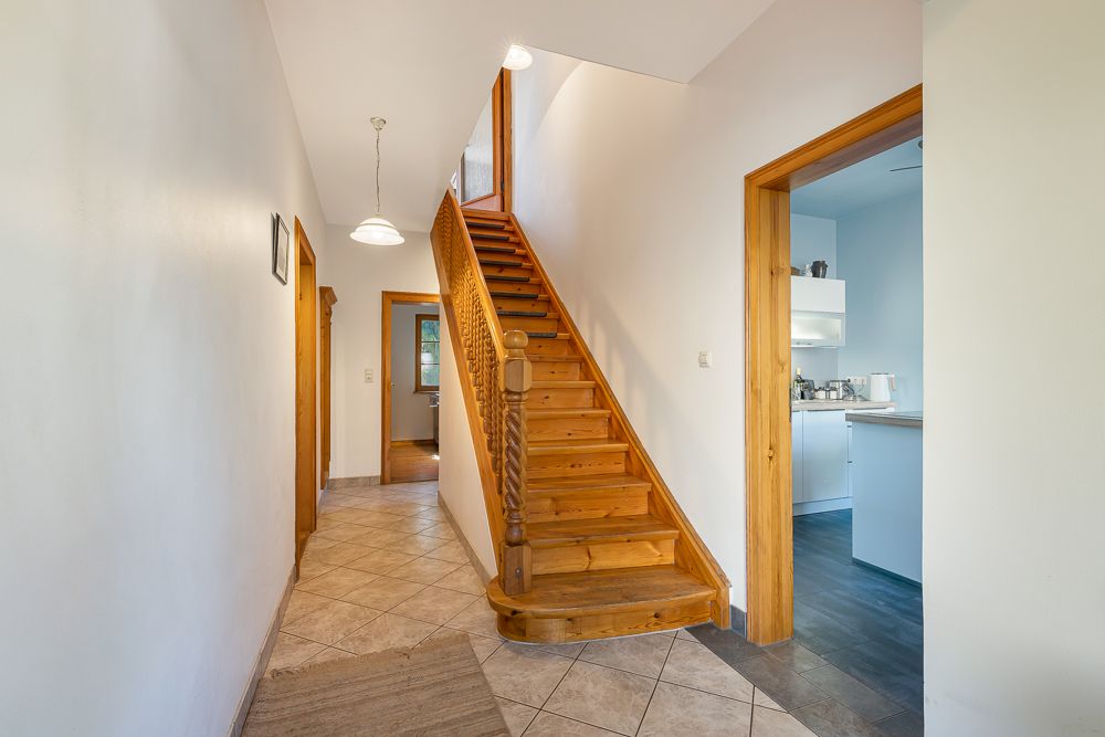 Flur mit Holztreppe, Fliesenboden und Zugang zu mehreren Zimmern.