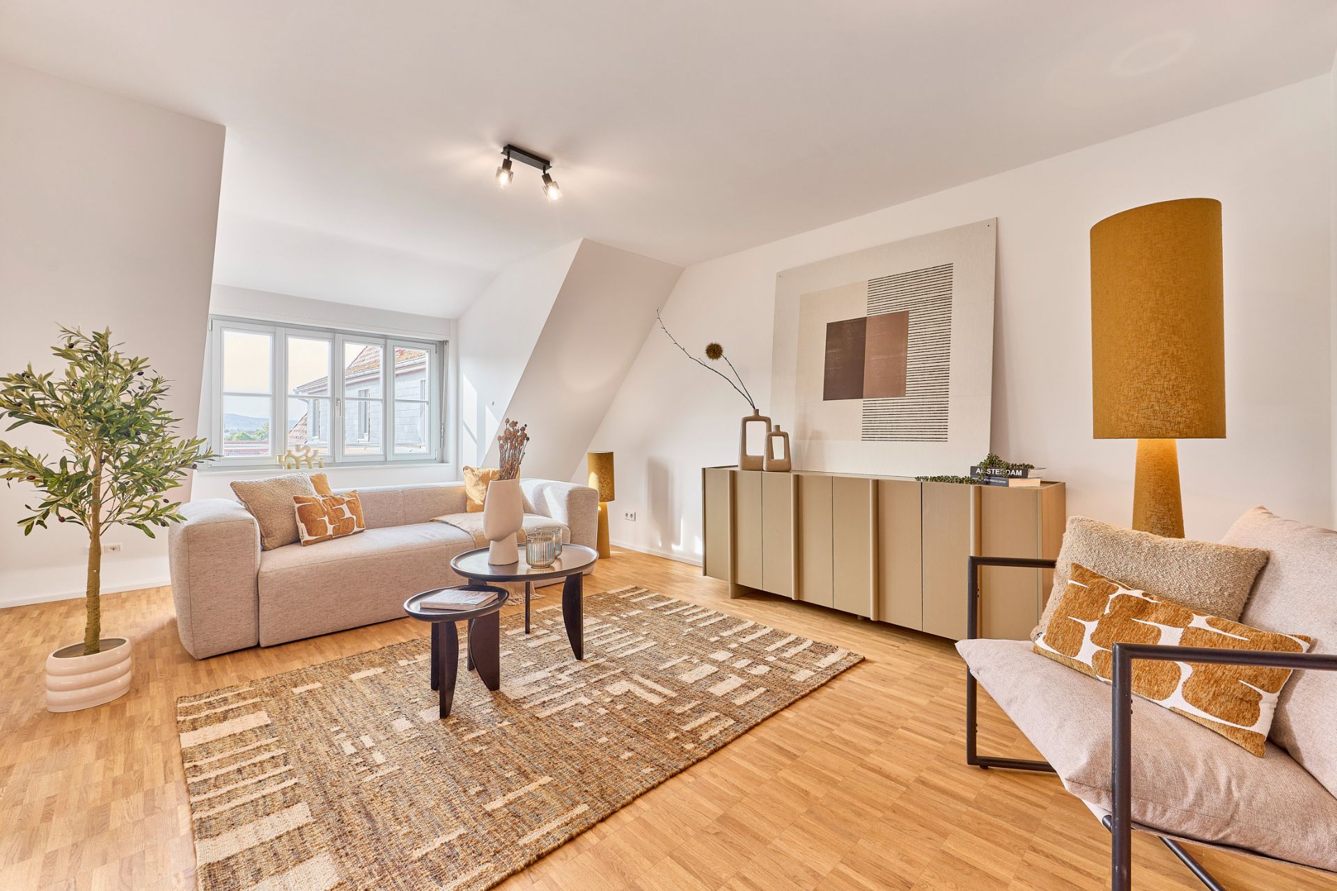 Helles Wohnzimmer mit Sofa, Sessel, Teppich, Sideboard, großen Fenstern und Dekoration.