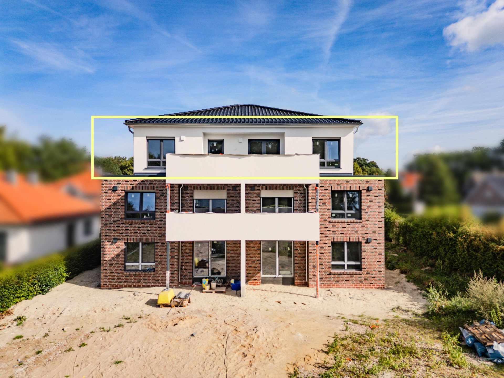 Dreistöckiges Wohnhaus mit Ziegelfassade und großen Fenstern, davor Sand und Garten.