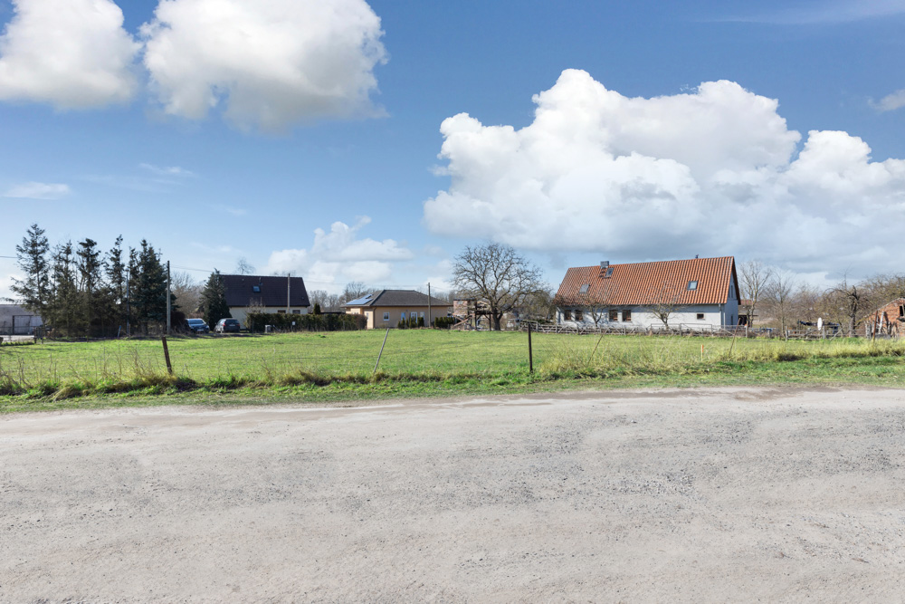 Großes grünes Feld mit mehreren Wohnhäusern im Hintergrund unter blauem Himmel.