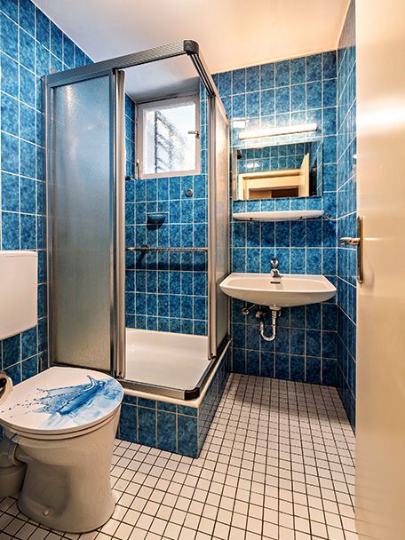 Kleines Badezimmer mit blauen Fliesen, Dusche, WC und Waschbecken mit Spiegel.