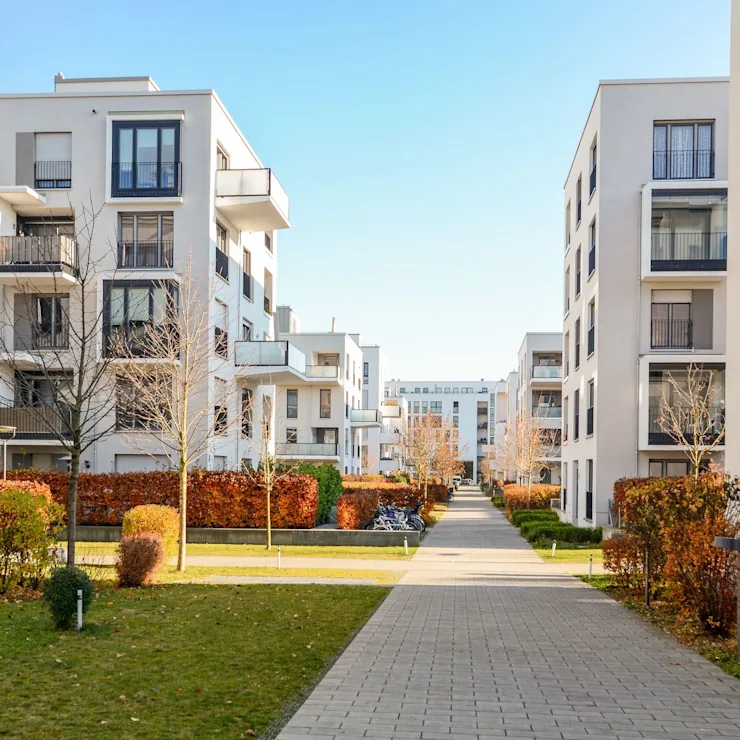 Moderne Wohngebäude mit Balkonen und einem Gehweg durch eine begrünte Anlage.