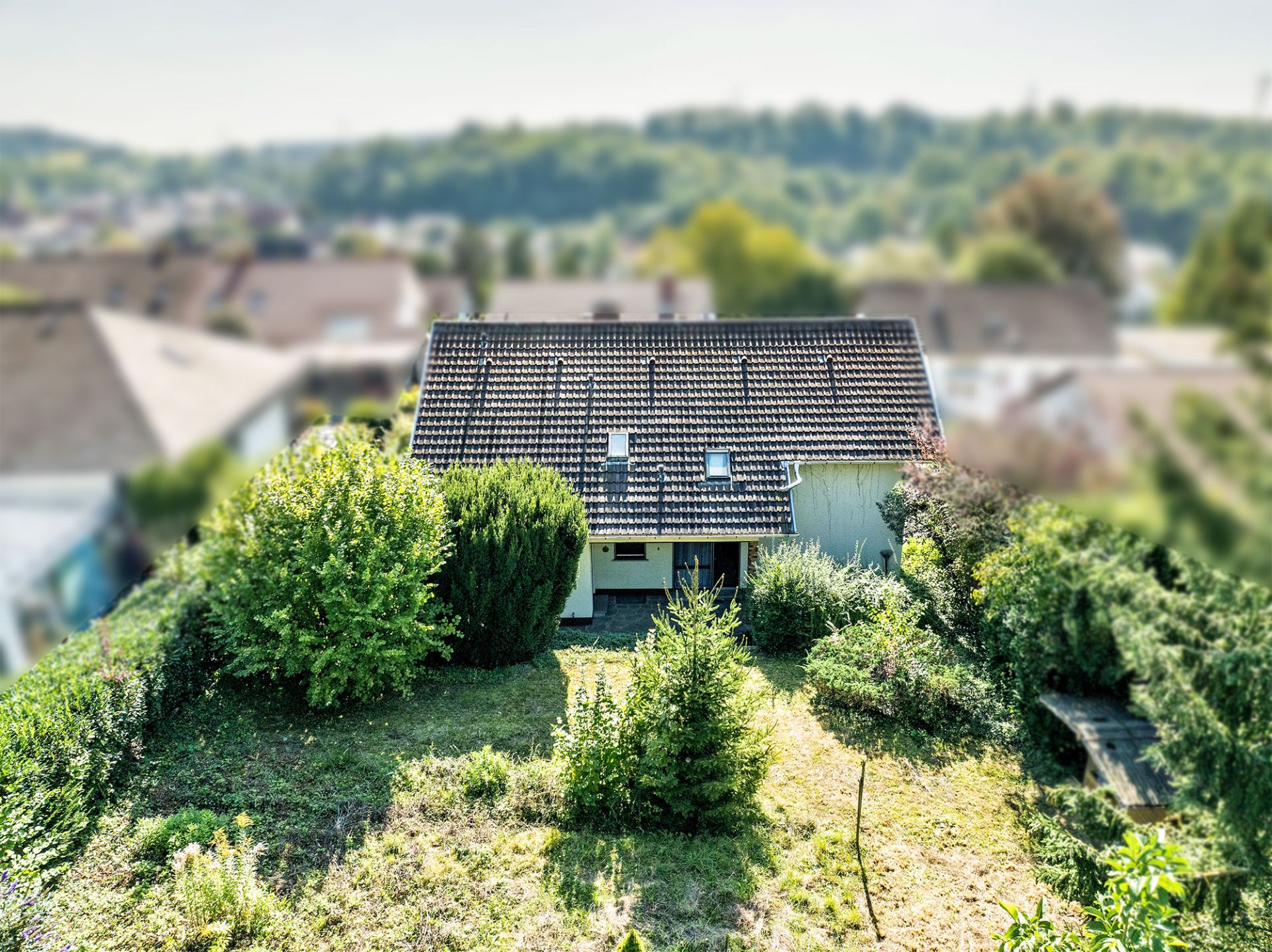 Einfamilienhaus mit dunklem Dach und umgebenem Garten, Blick aus erhöhter Position.