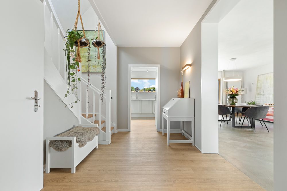 Heller Flur mit Holzfußboden, Treppe, Sitzbank, Hängepflanzen und Blick ins Esszimmer.