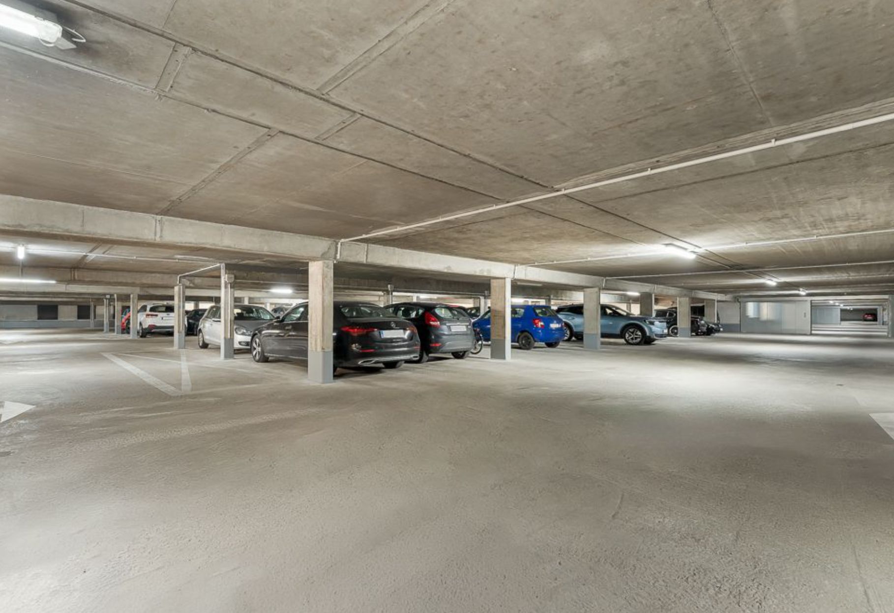 Tiefgaragenparkplatz mit mehreren Autos und Betonstützen unter beleuchtetem Decken.