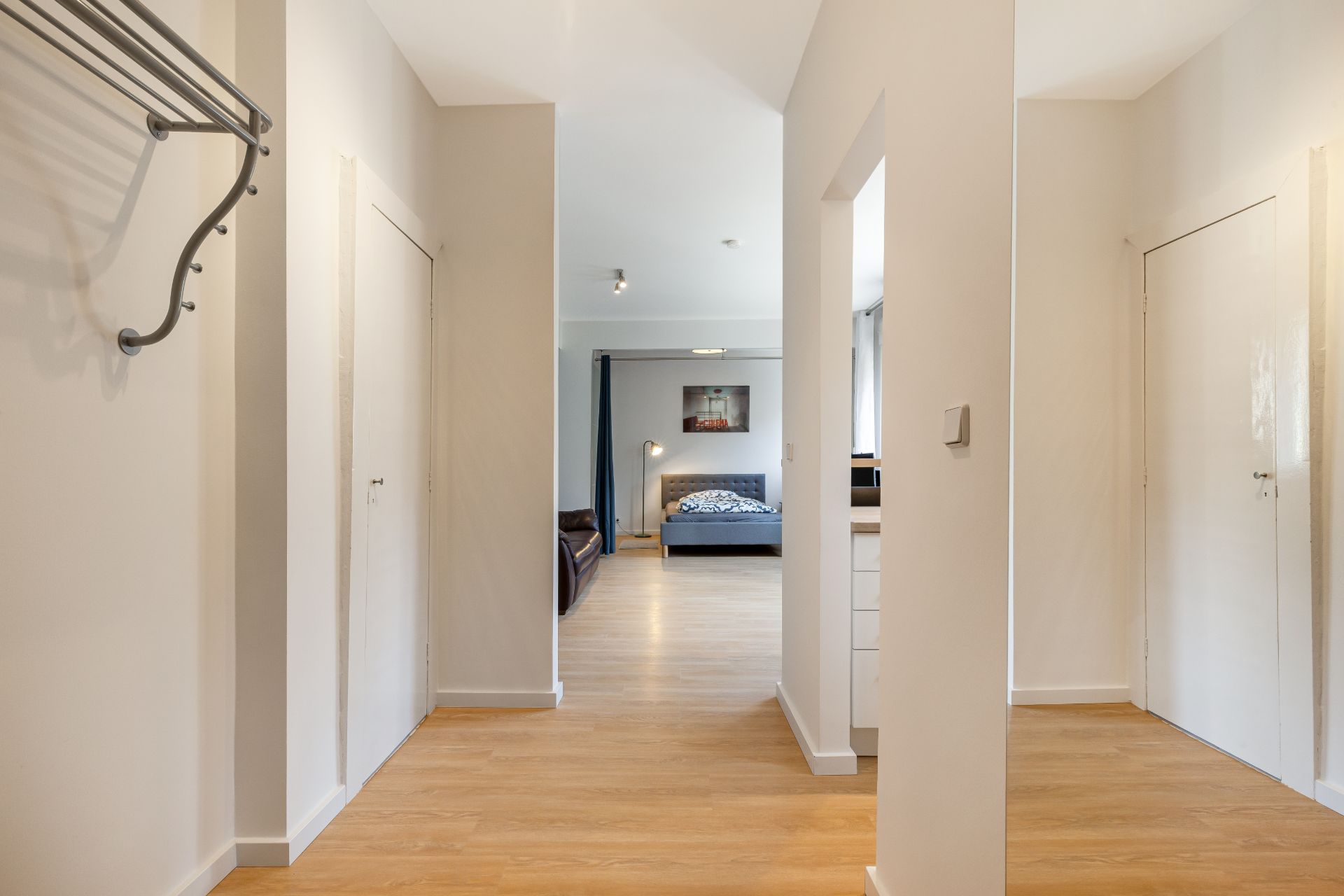 Heller Flur mit Holzboden, Türen und Blick auf ein Schlafzimmer.