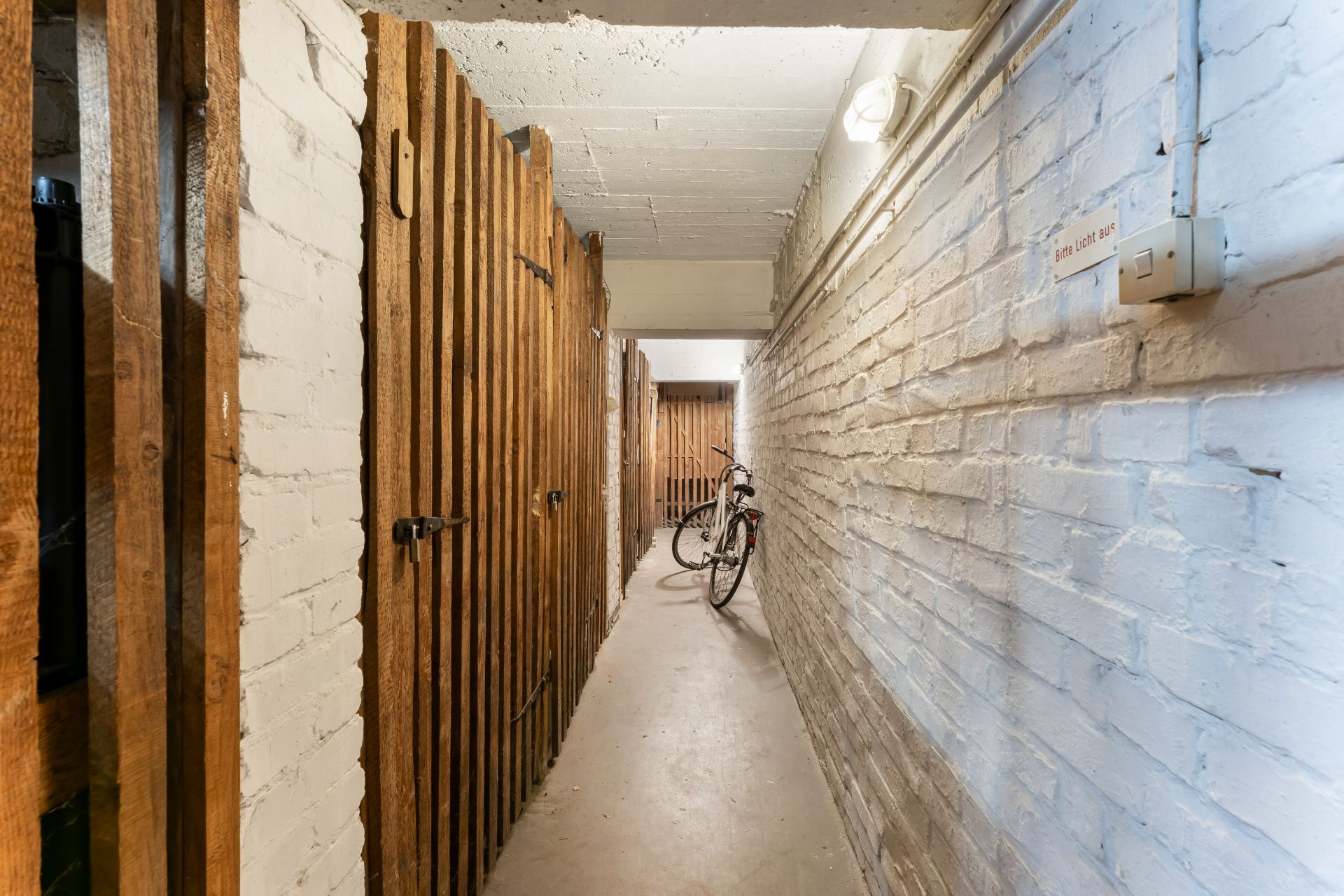 Schmaler Kellerflur mit abschließbaren Holzgittern und einem abgestellten Fahrrad.