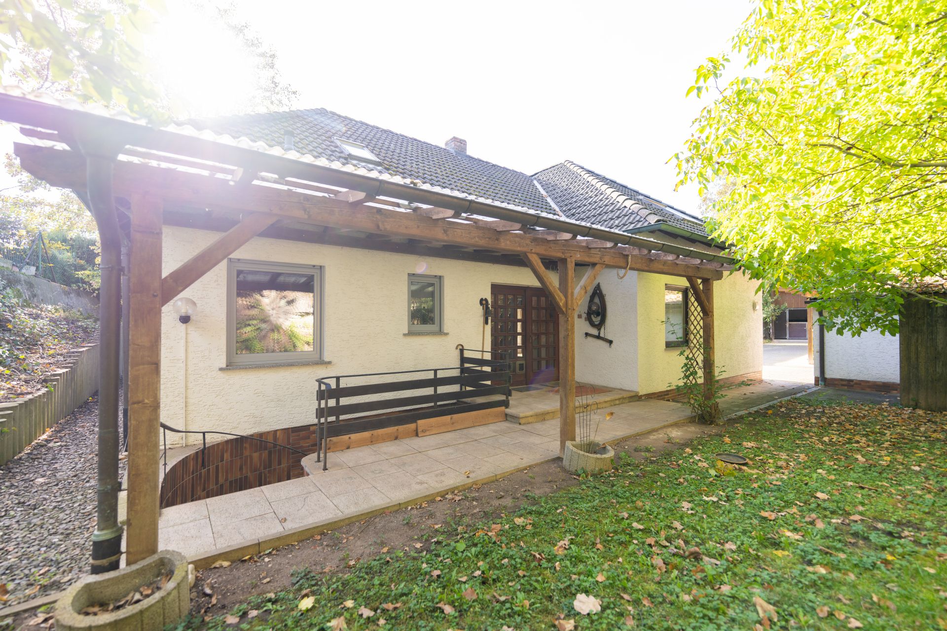 Einfamilienhaus mit überdachter Terrasse, kleinem Garten und Rampe zum Eingang.