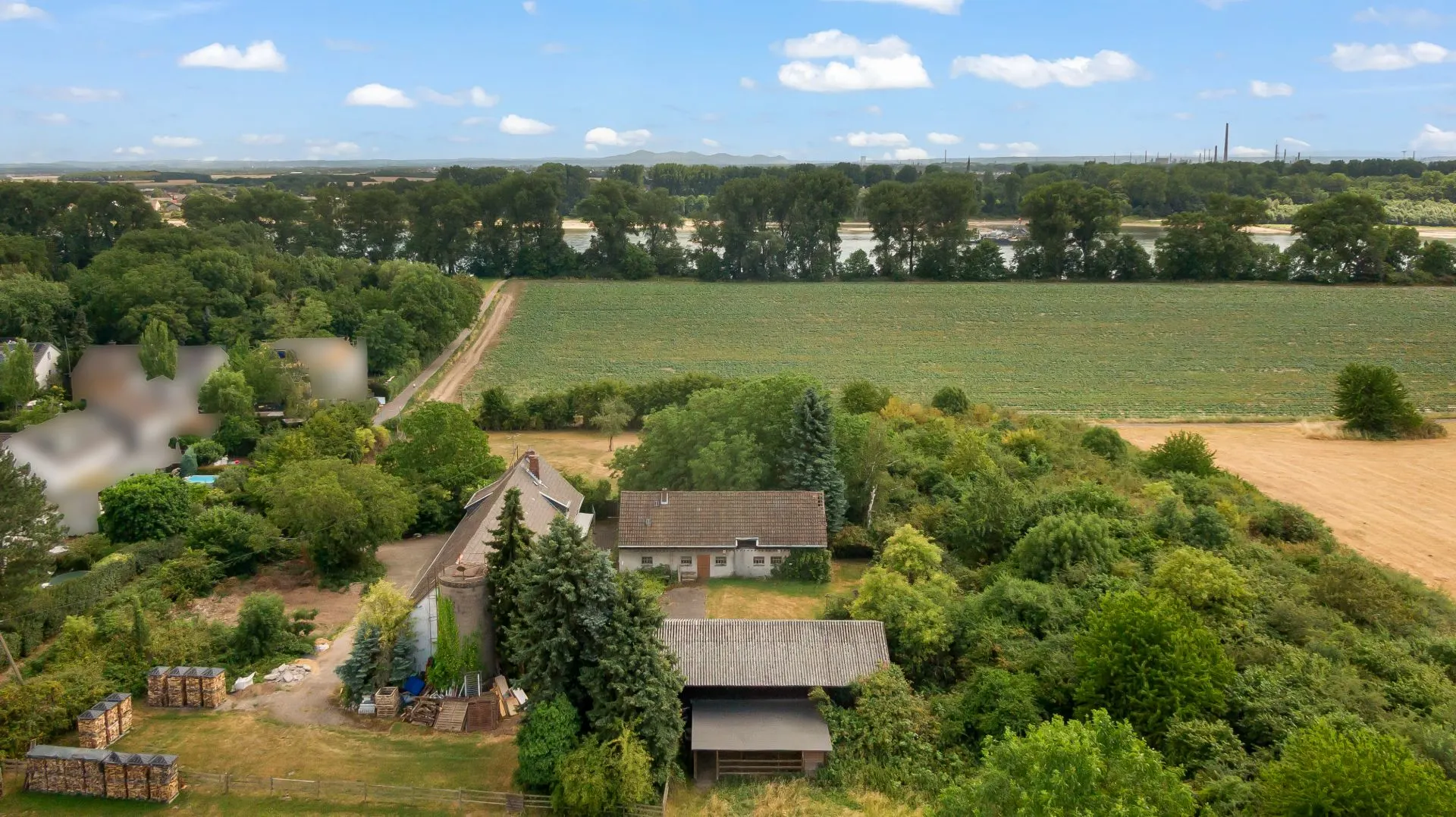 Luftaufnahme eines Hauses mit Nebengebäuden, umgeben von Feldern und vielen Bäumen.