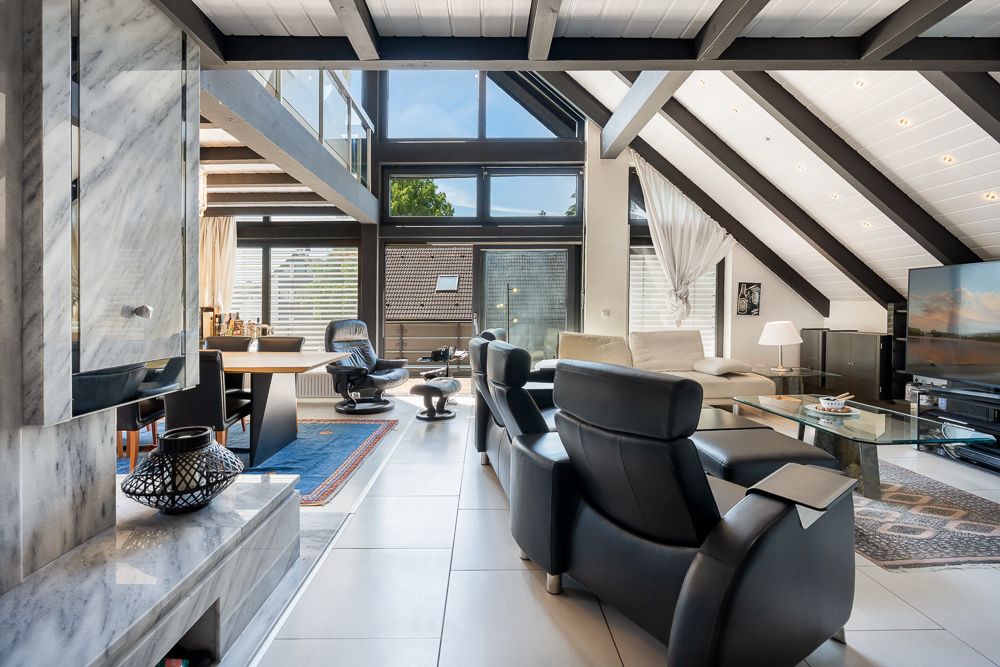 Modernes Wohnzimmer mit hohen Decken, großen Fenstern, Ledersesseln und Glas-Couchtisch.
