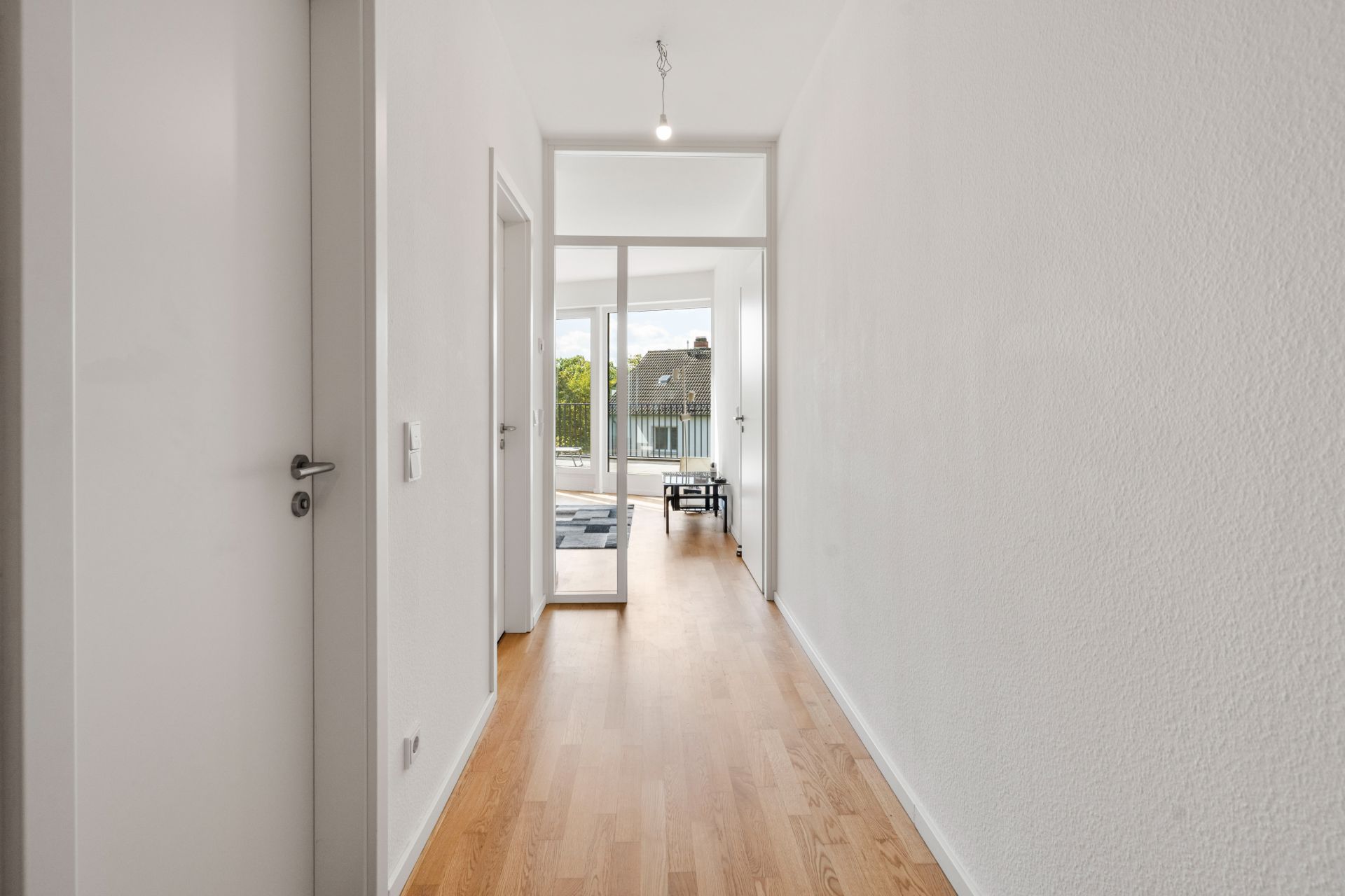 Heller Flur mit Holzboden, weißen Wänden und Glastür am Ende.