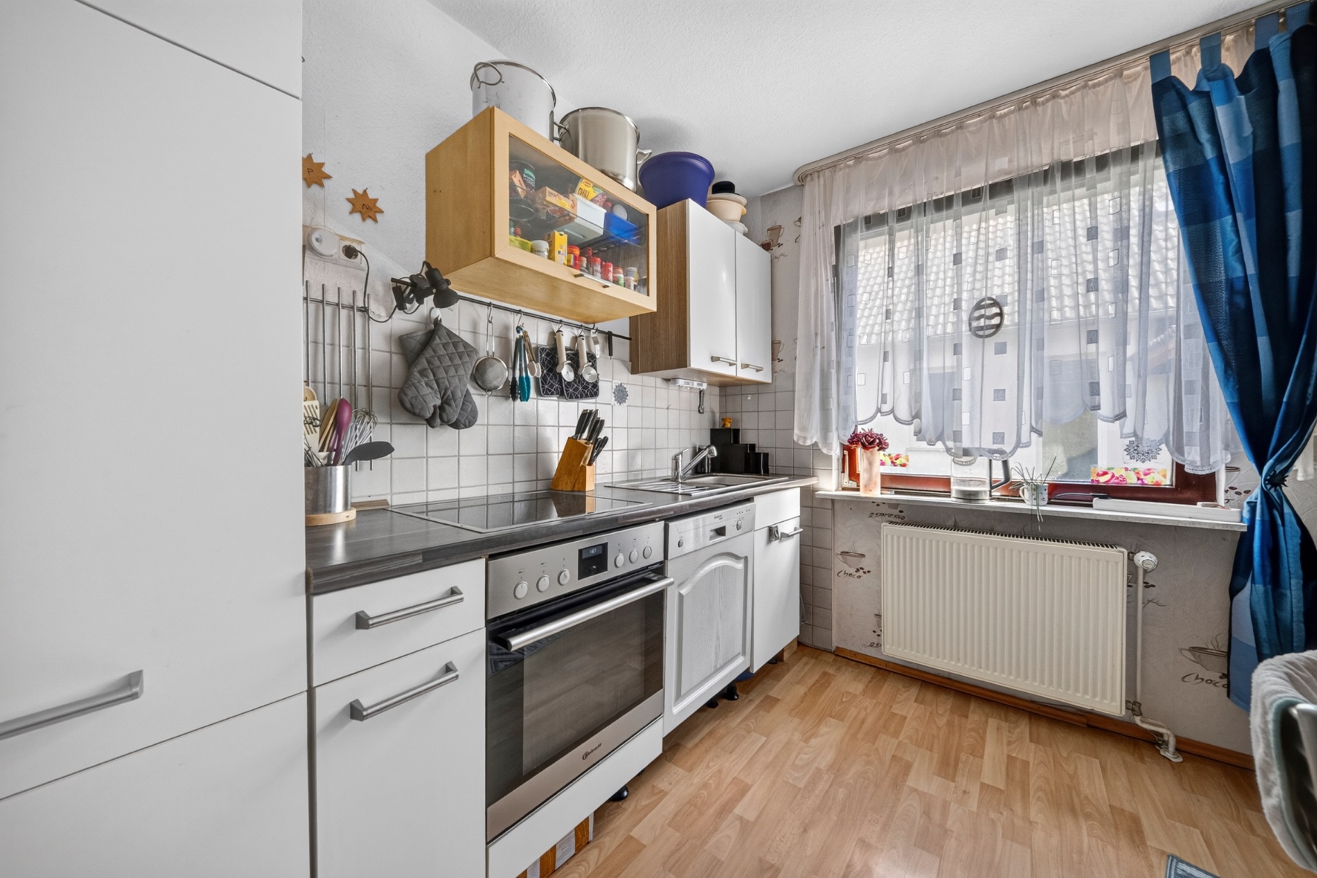 Helle Küche mit Herd, weißen Schränken, Holzfußboden und Fenster mit Vorhängen.