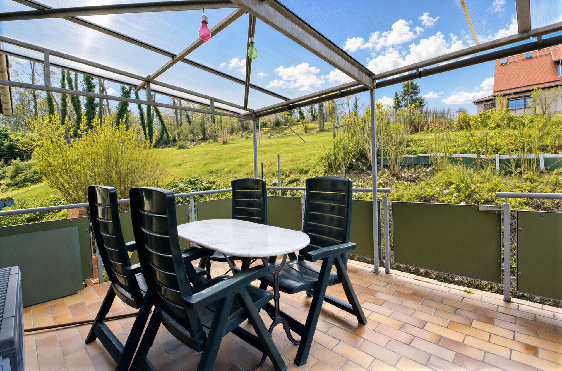 Überdachte Terrasse mit Tisch und fünf Stühlen, Blick auf grünen Garten und Wiese.