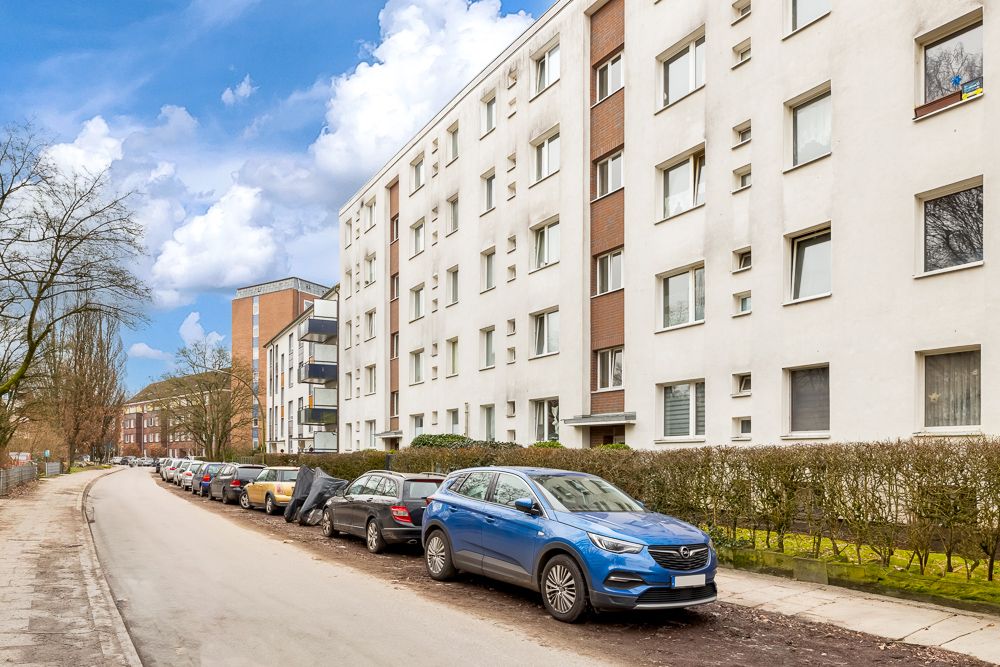 Mehrstöckiges Wohngebäude mit geparkten Autos entlang einer ruhigen Straße.