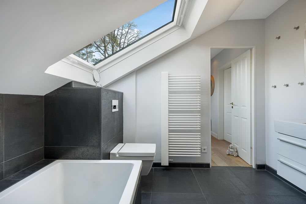 Modernes Badezimmer mit Badewanne, WC, Dachfenster und weißem Handtuchheizkörper.