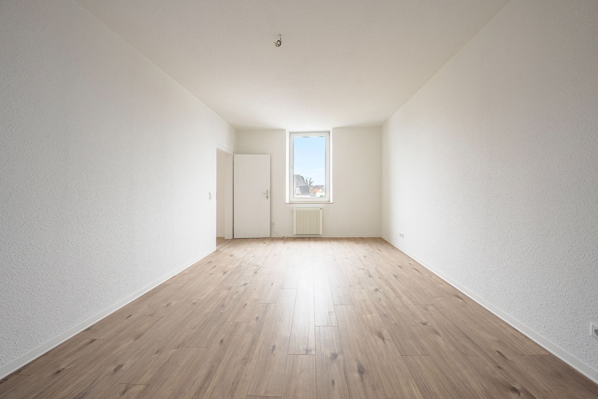 Leeres, helles Zimmer mit Holzfußboden, weißer Wand, Fenster und Tür.
