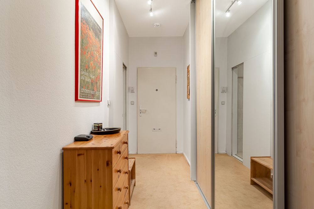 Heller Flur mit Holzkommode, Spiegel und weißer Tür.