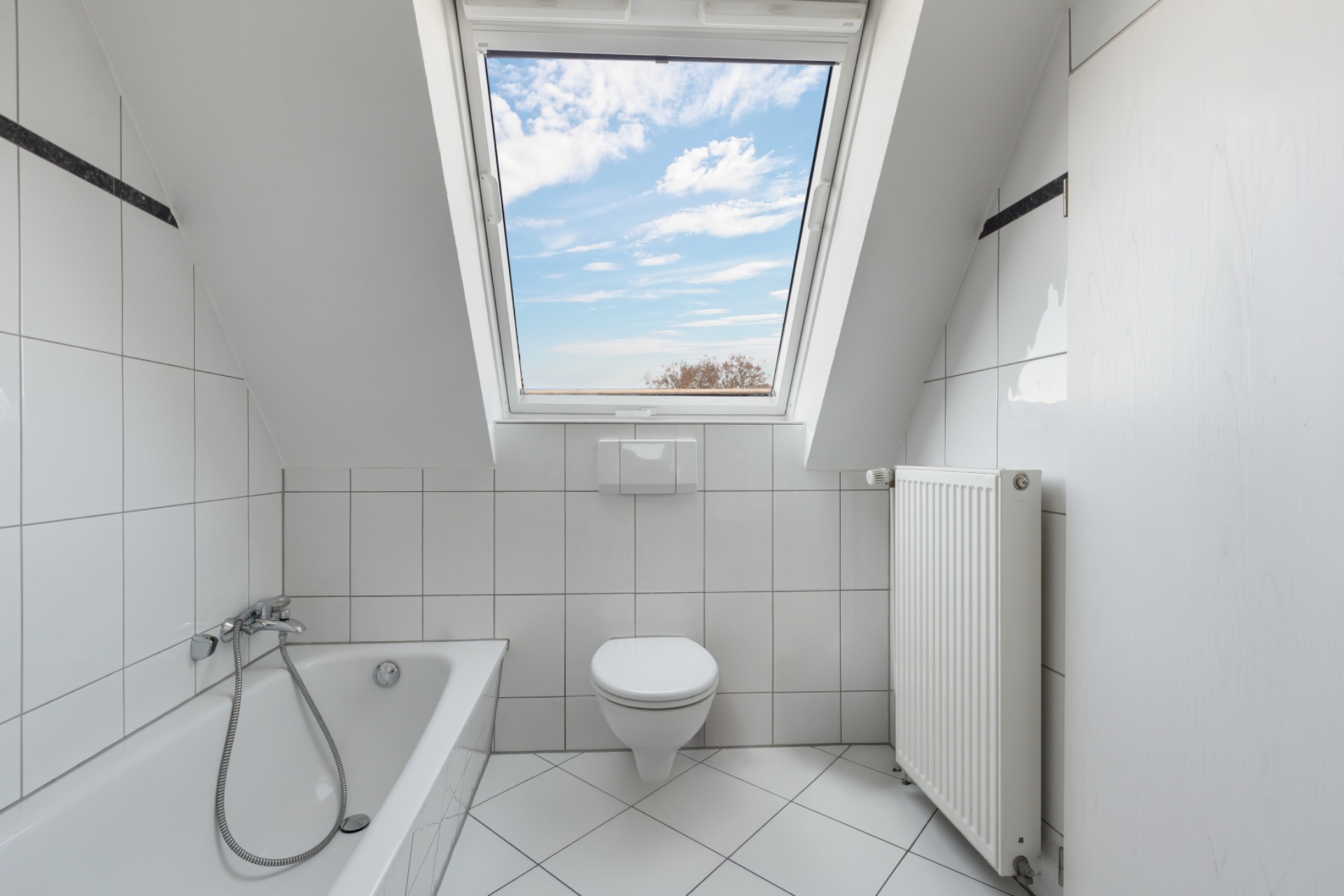 Modernes Badezimmer mit Badewanne, Toilette und Dachfenster unter einer Schräge.