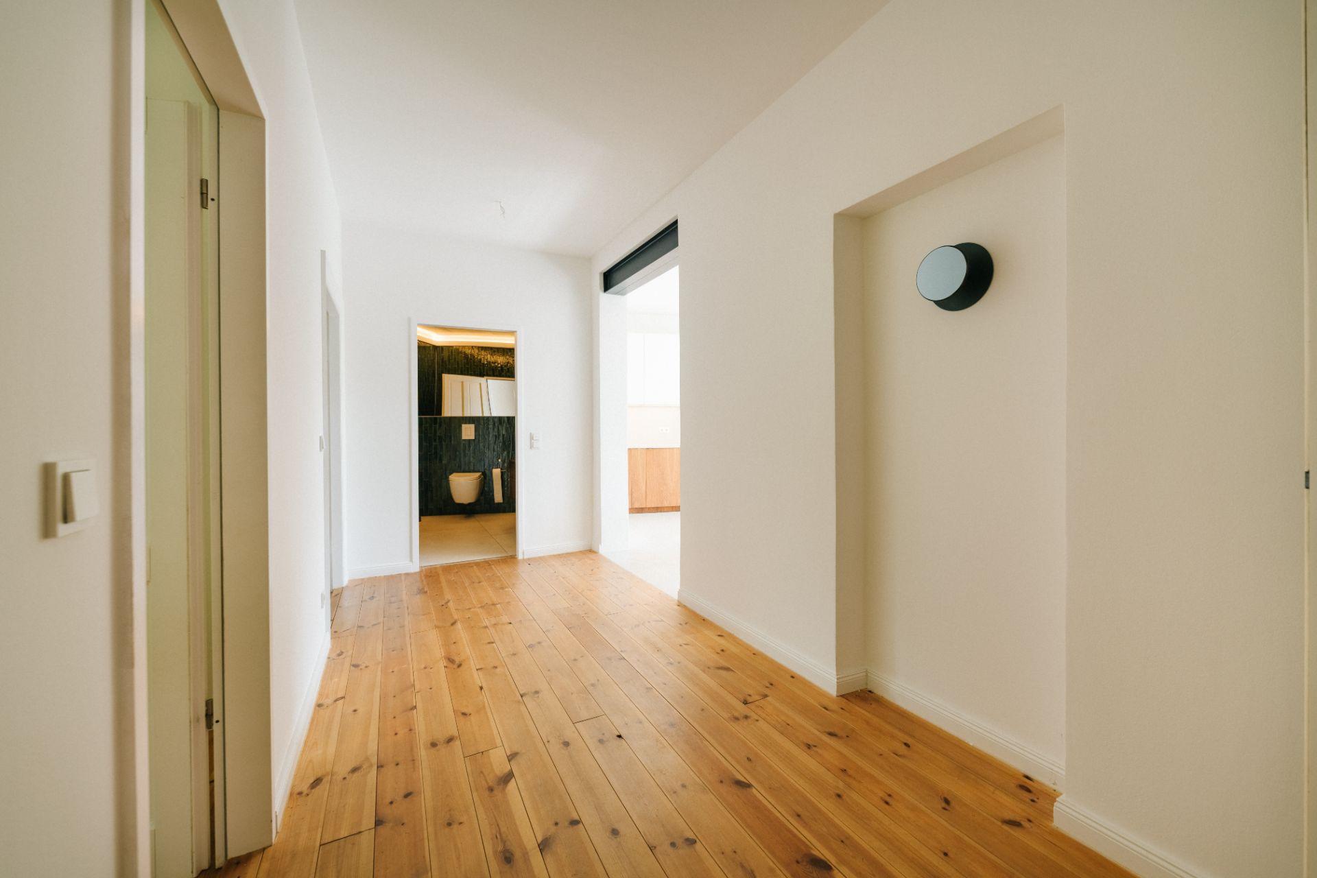 Heller Flur mit Holzboden, Türen an den Seiten und Blick in ein Badezimmer mit Toilette.