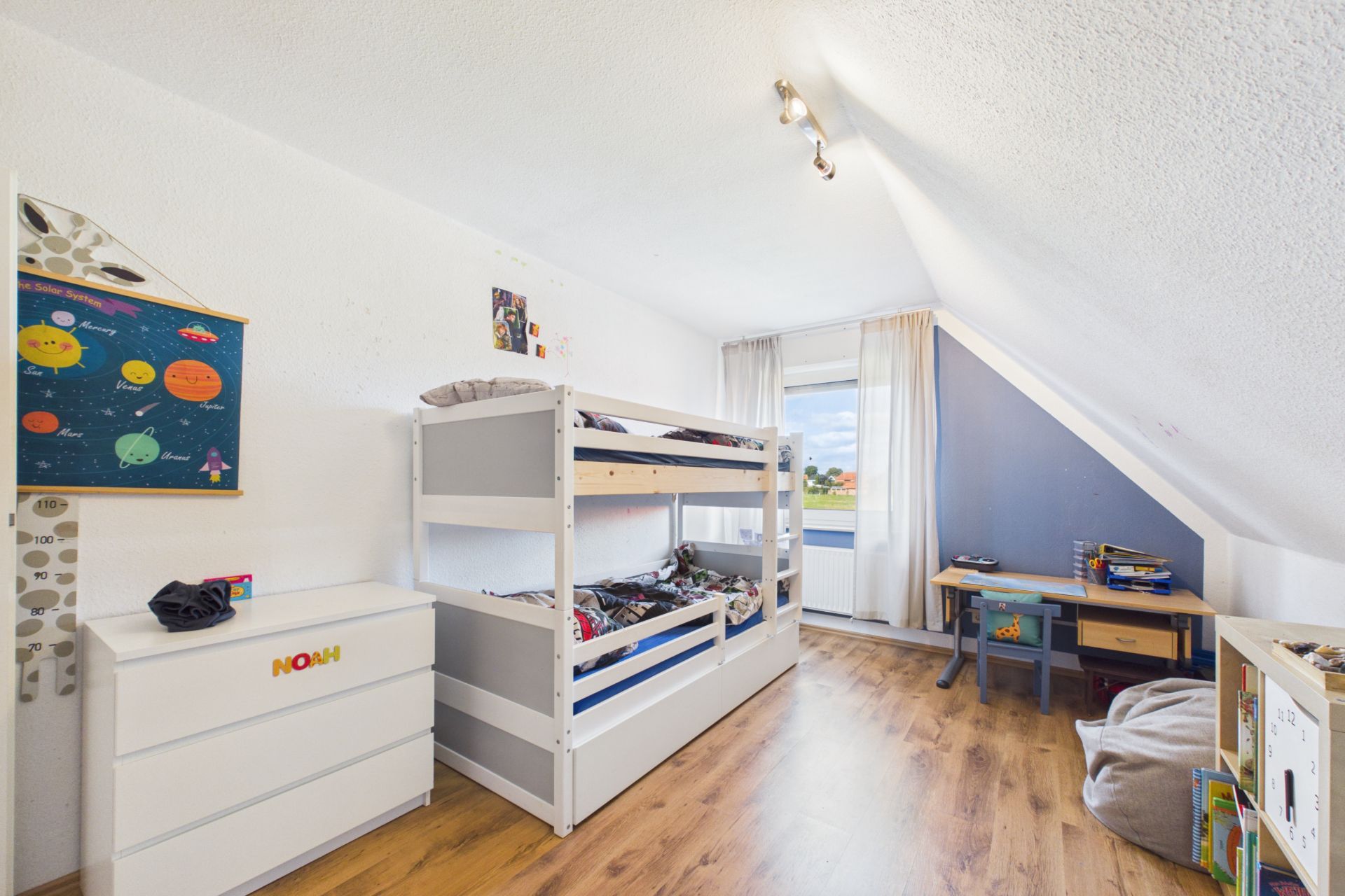 Kinderzimmer mit Etagenbett, Schreibtisch, Kommode und Spielsachen auf Holzfußboden unter Dachschräge.
