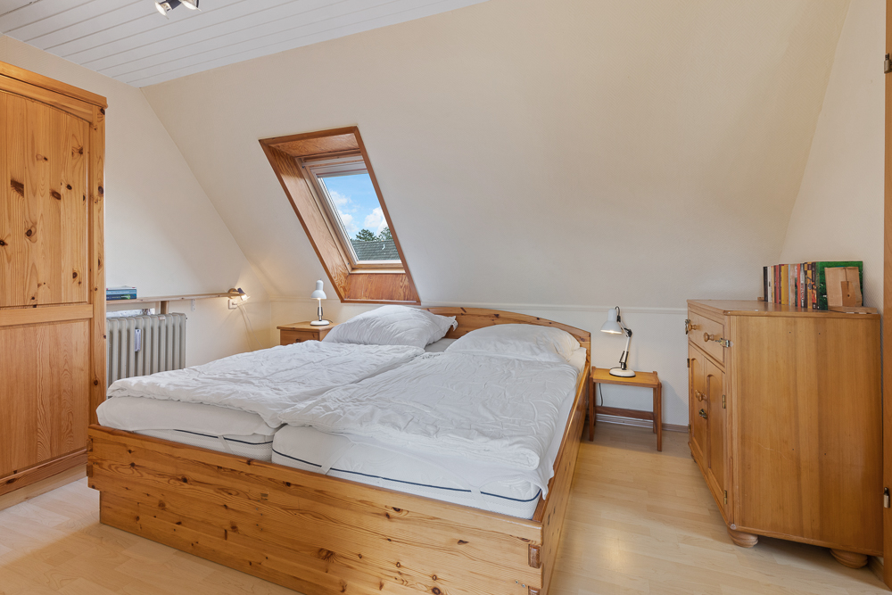 Helles Schlafzimmer mit Doppelbett, Holzmöbeln und Dachfenster.