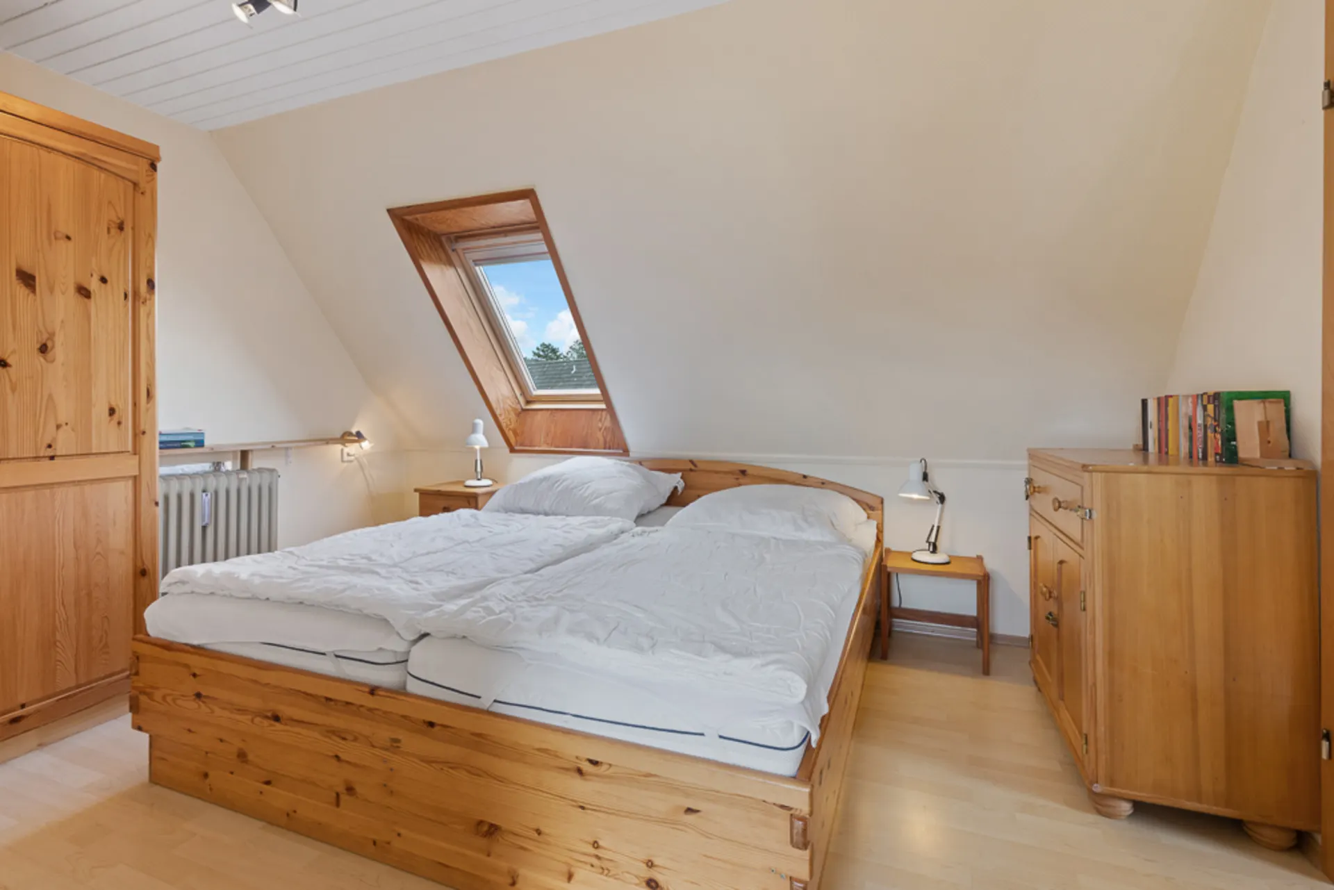 Helles Schlafzimmer mit Doppelbett, Holzmöbeln und Dachfenster.