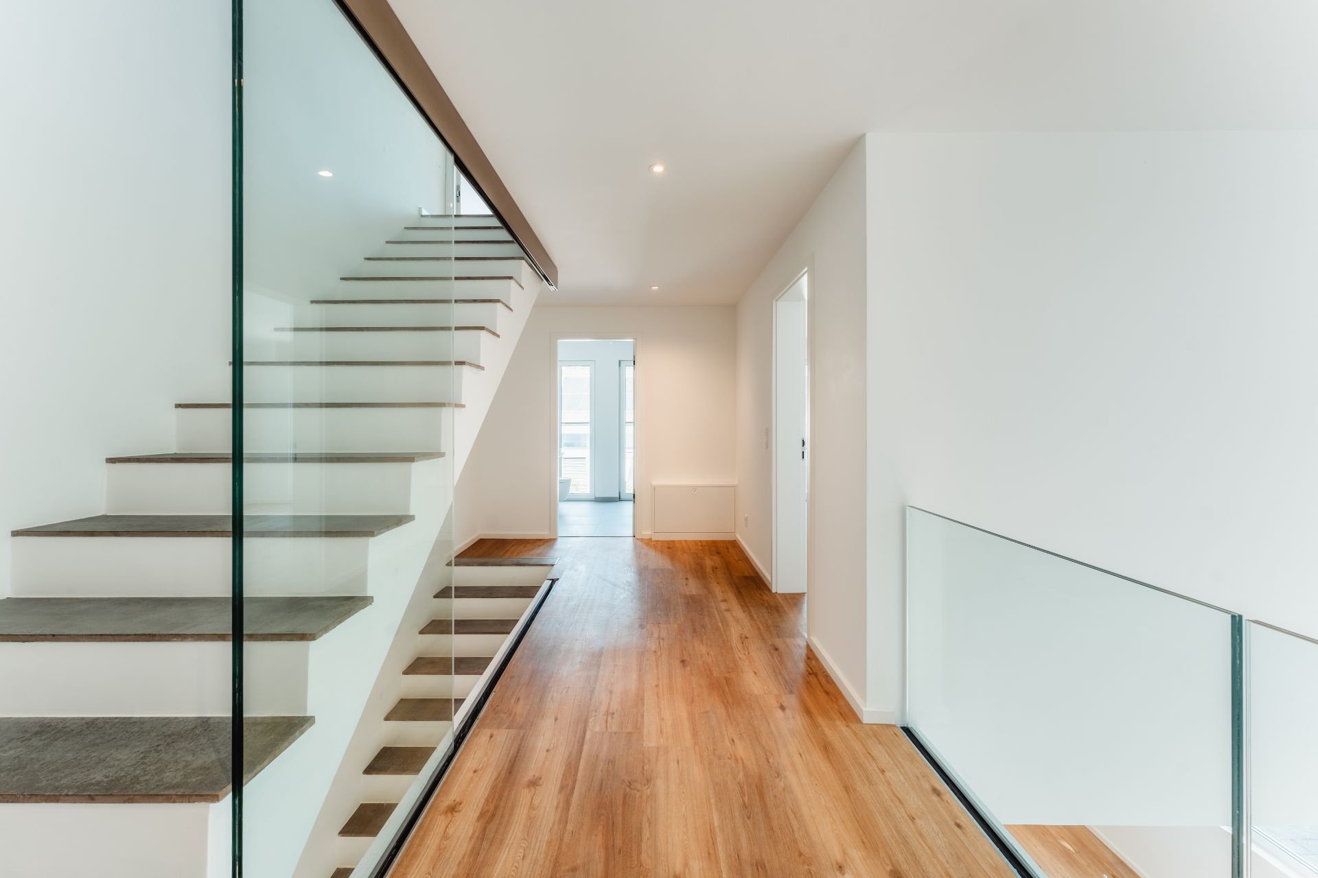 Heller Flur mit Holzfußboden und moderner Treppe mit Glasgeländer.