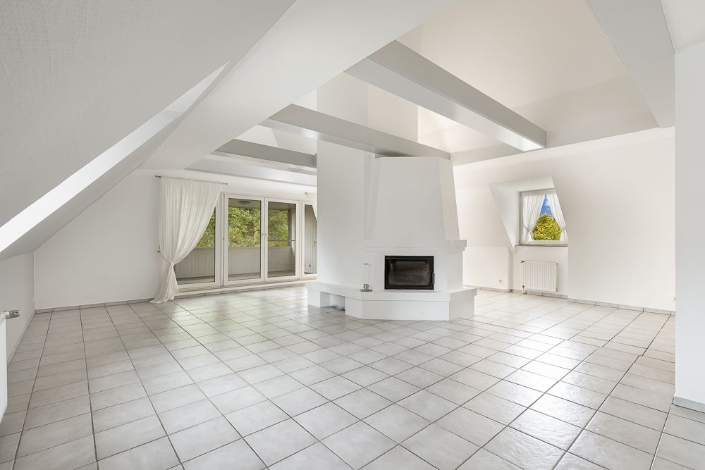 Helles Wohnzimmer mit Kamin, großen Fenstern, Fliesenboden und sichtbaren Dachbalken.