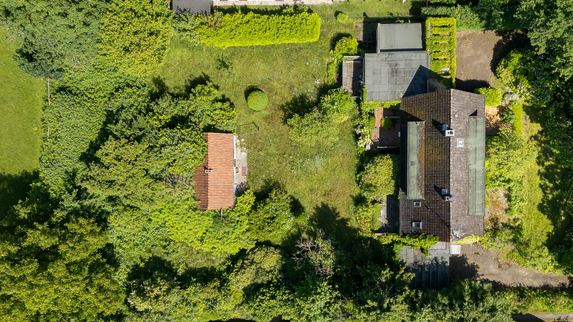 Luftaufnahme eines Wohnhauses mit Nebengebäude und großem Garten, umgeben von Bäumen.
