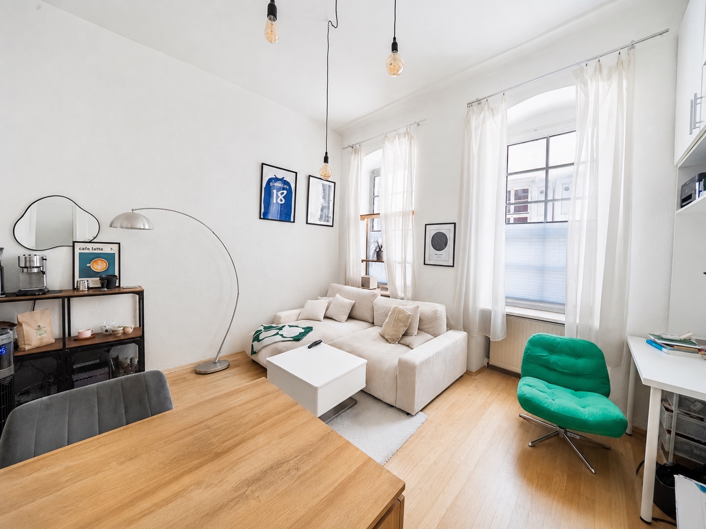Helles Wohnzimmer mit weißem Sofa, grünem Sessel, großem Fenster und Holzboden.