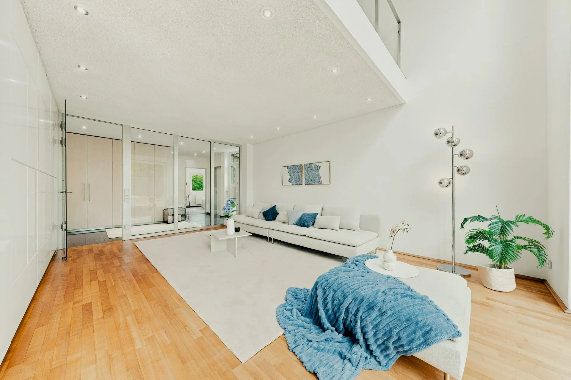 Modernes, helles Wohnzimmer mit weißem Sofa, Holzboden und großen Glaswänden.