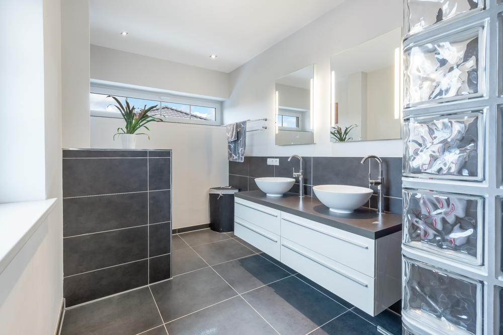 Modernes Badezimmer mit zwei Waschbecken, großen Spiegeln, Glasbausteinen und grauen Fliesen.