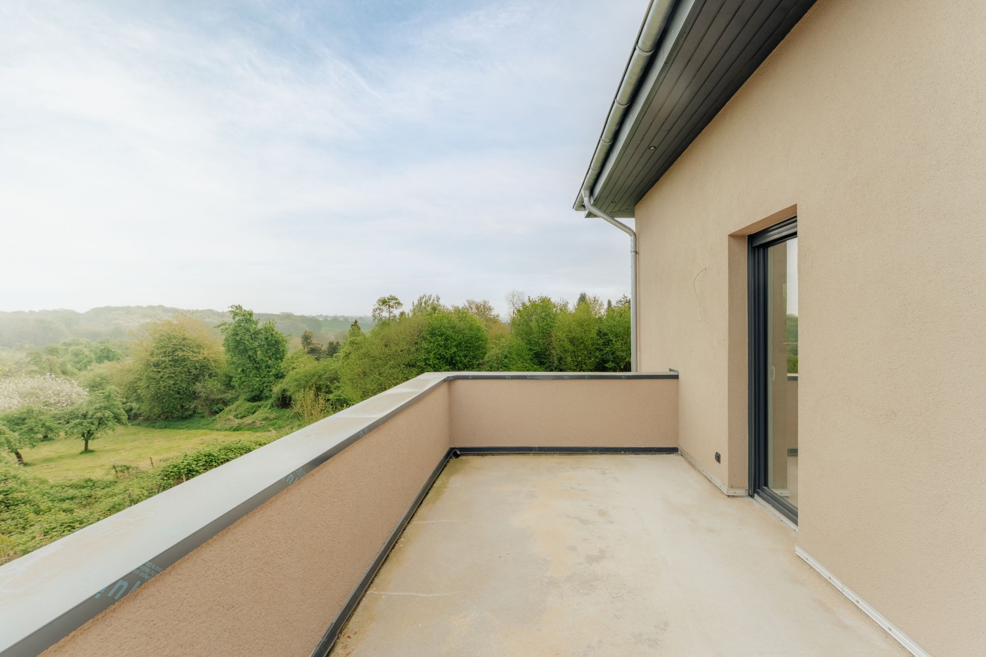 Balkon mit cremefarbenem Boden und Geländer, Blick auf grüne Bäume und Landschaft.