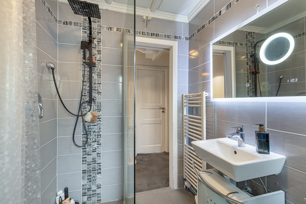 Modernes Badezimmer mit Dusche, Waschbecken, großem Spiegel und Handtuchheizkörper.