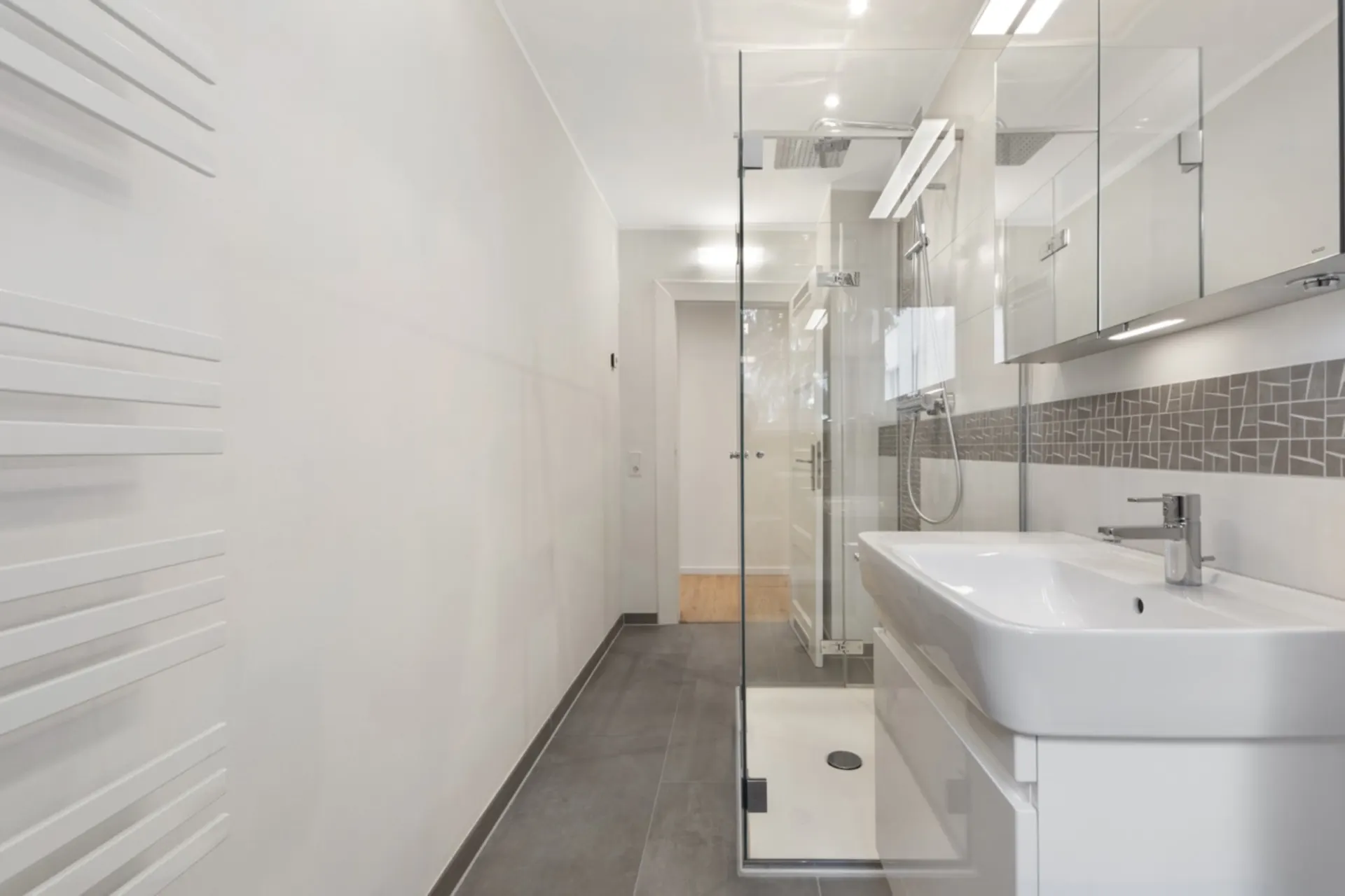 Modernes Bad mit Dusche, großem Waschbecken und Spiegeln, graue Fliesen und Handtuchheizkörper.