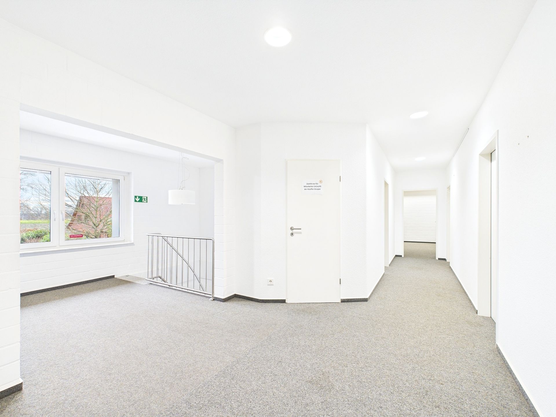 Heller Flur mit mehreren Türen, Fenster und Treppengeländer auf der linken Seite.