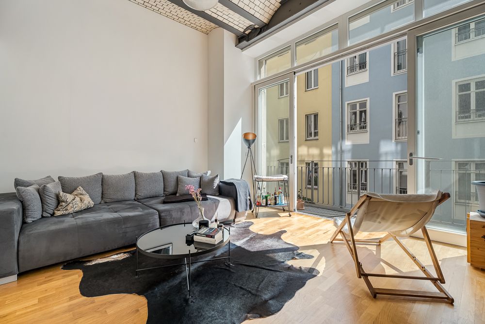 Helles Wohnzimmer mit grauem Sofa, Sessel, Couchtisch und großen Fenstern zu einem Balkon.