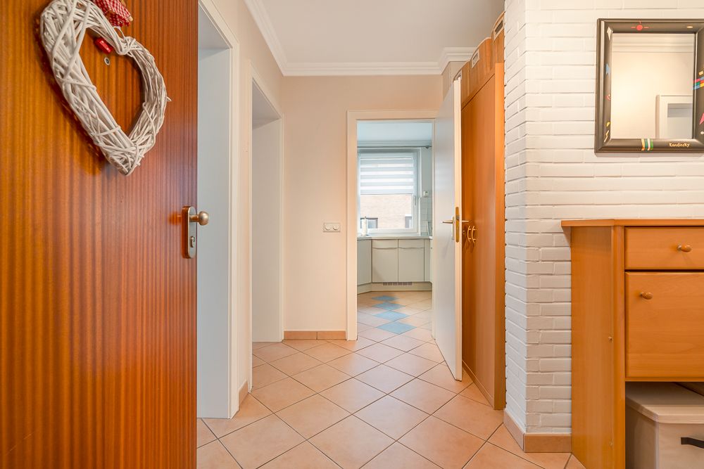 Heller Flur mit Fliesenboden, Holztüren und Blick in eine Küche mit Fenster.