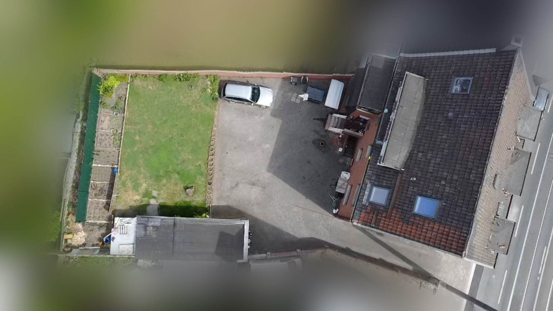 Luftaufnahme von Haus, Garten, Einfahrt und geparktem Auto auf einem Grundstück.
