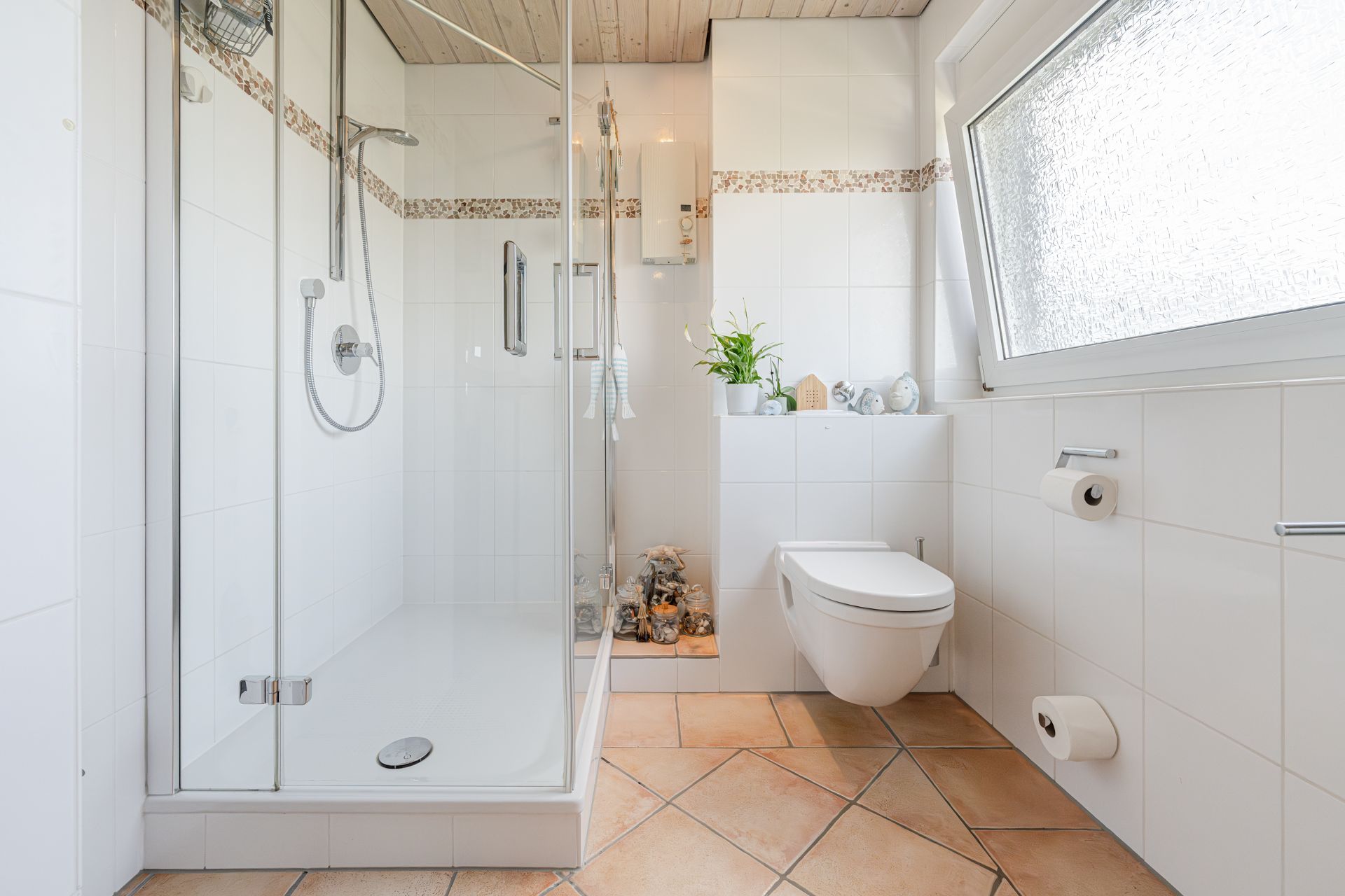 Helles Bad mit begehbarer Dusche, Wandtoilette, Deko und großem Fenster.