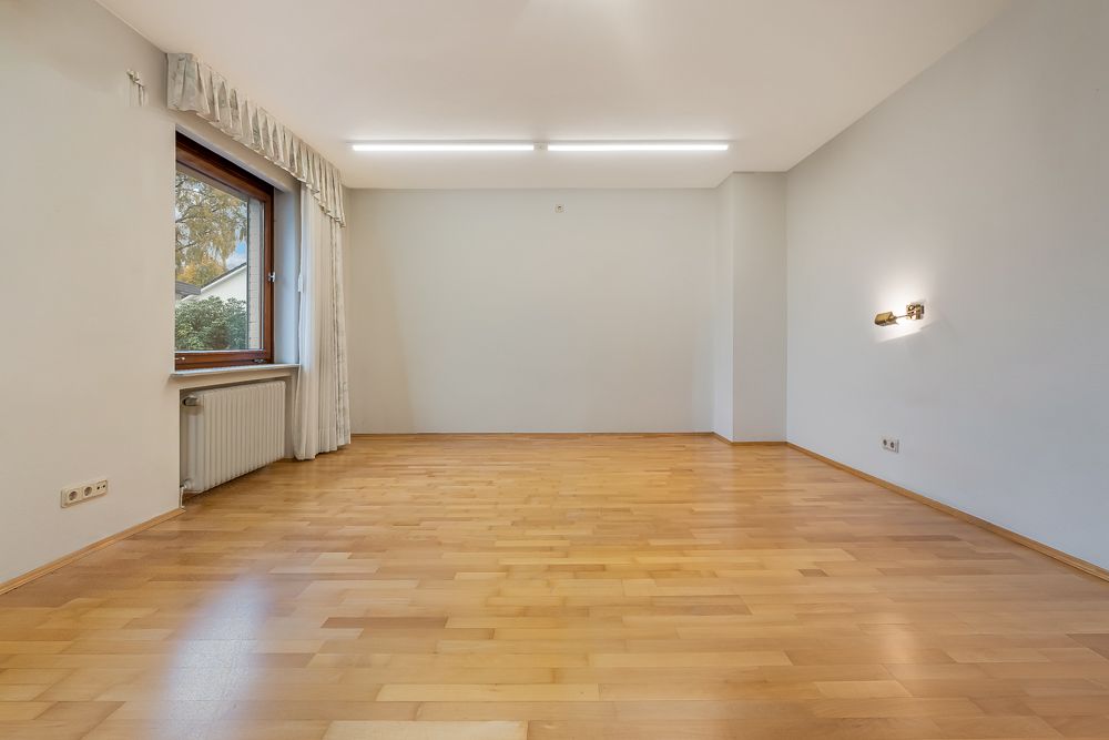 Leerer Raum mit hellem Holzfußboden, großem Fenster, weißen Wänden und Deckenleuchte.