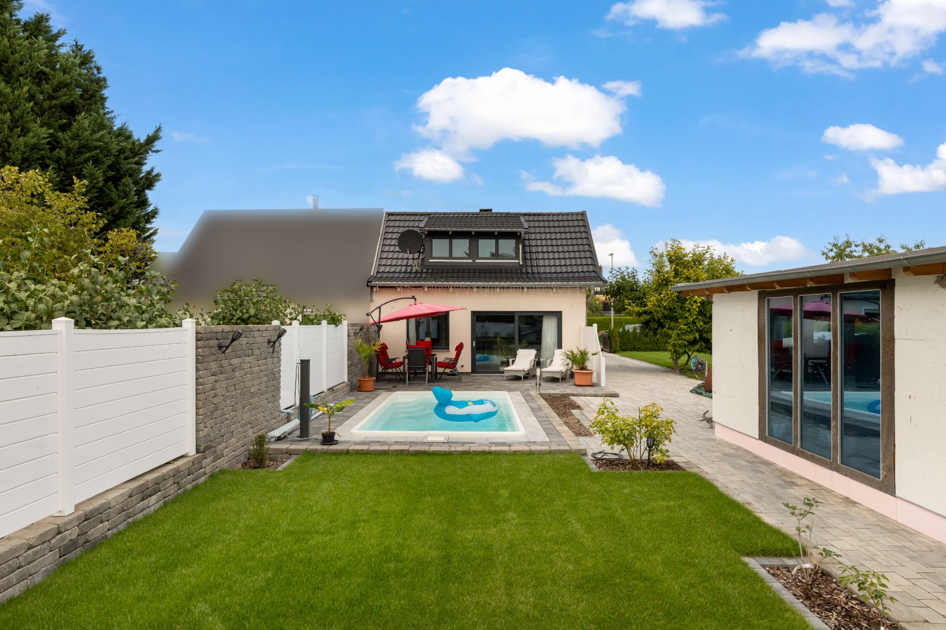 Garten mit kleinem Pool, aufblasbarem Spielzeug, Terrasse und modernem Einfamilienhaus im Hintergrund.