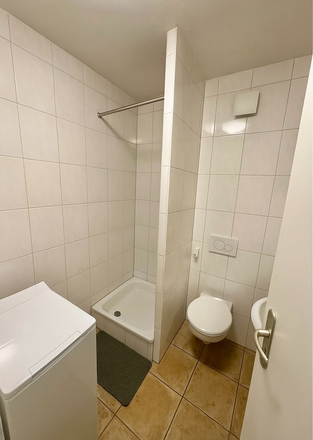 Kleines Badezimmer mit Dusche, Waschmaschine, Wand-WC und Waschbecken.