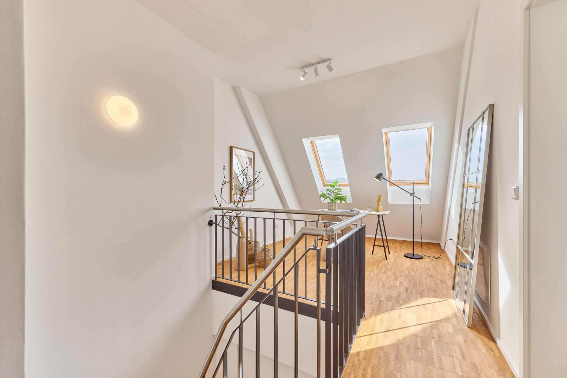 Helle Galerie mit Holzfußboden, Geländer, zwei Fenstern und Stehlampe.