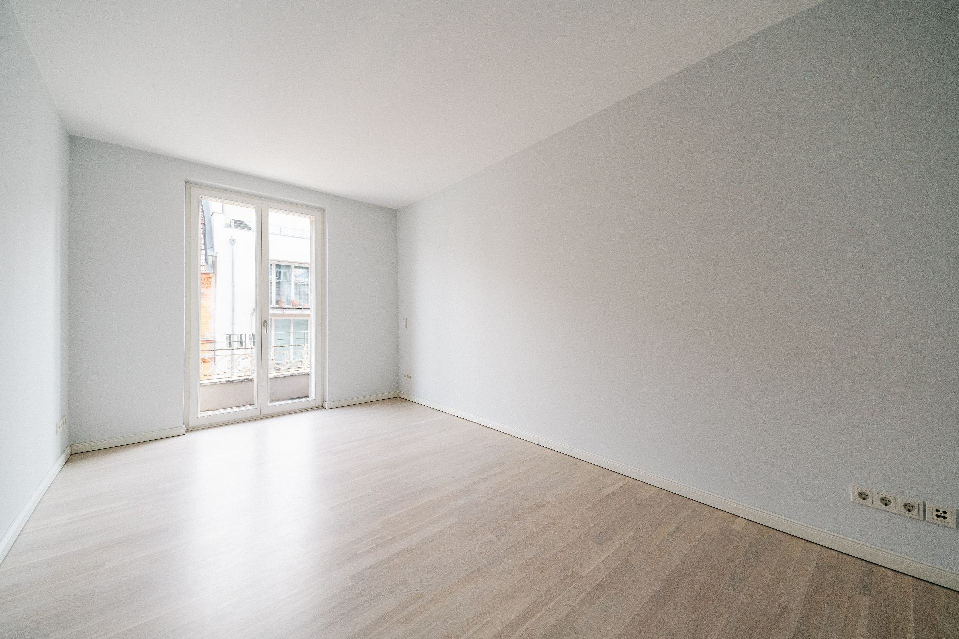 Heller, leerer Raum mit Holzfußboden und großen Fenstertüren zu einem Balkon.