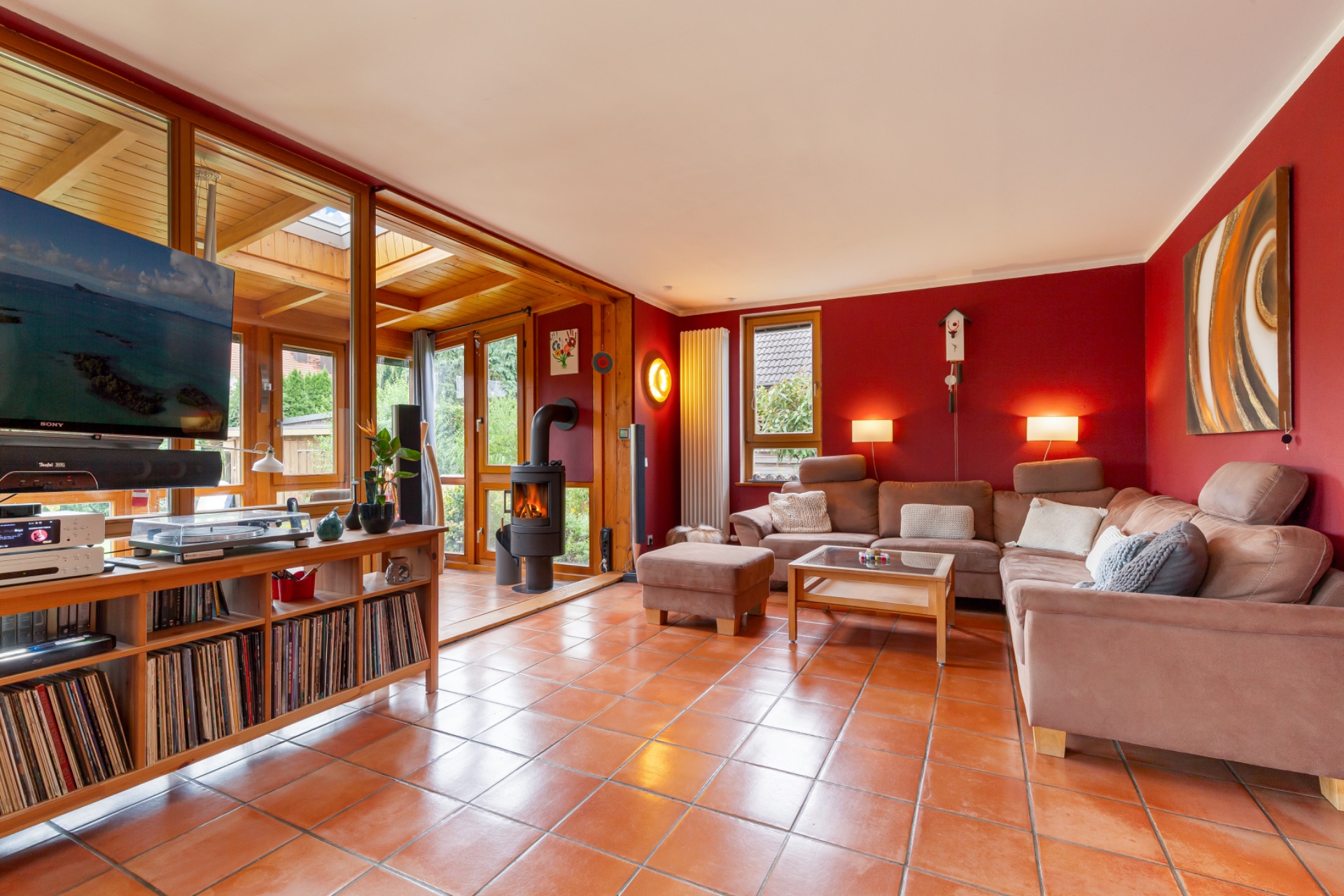 Wohnzimmer mit braunen Sofas, Holzmöbeln, Kamin und großen Fenstern zum Wintergarten.