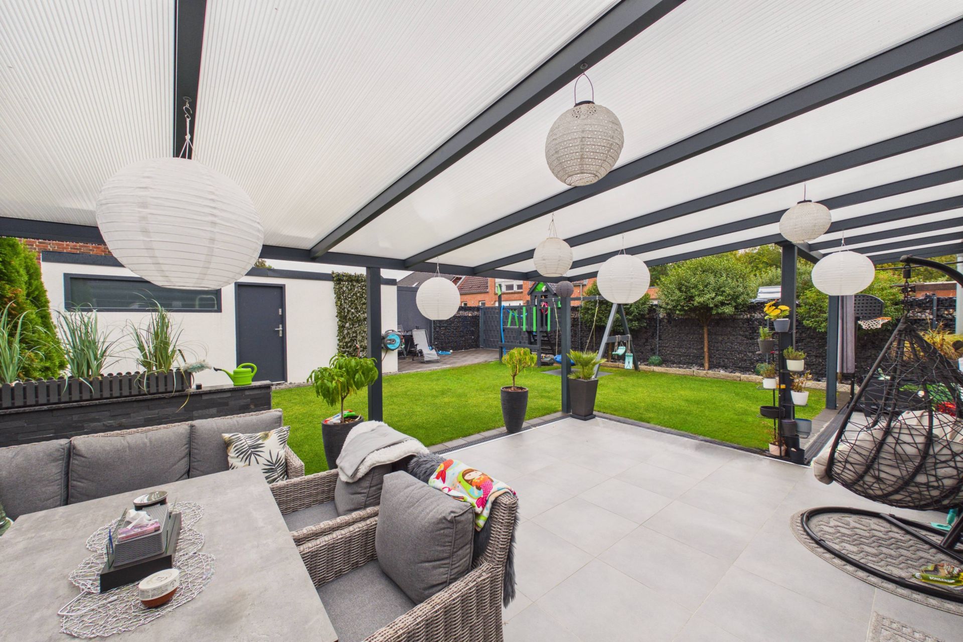Überdachte Terrasse mit Sitzgruppe, Lampions und Blick auf grünen Garten.